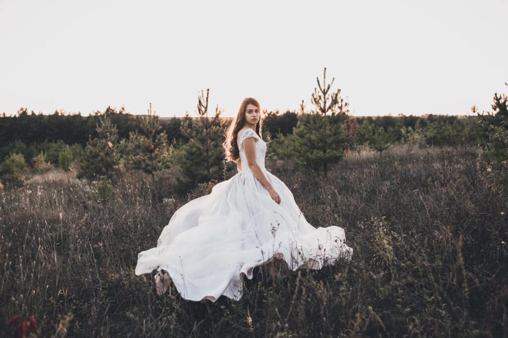 bride in wedding white dress walking on meadow in summer at sunset