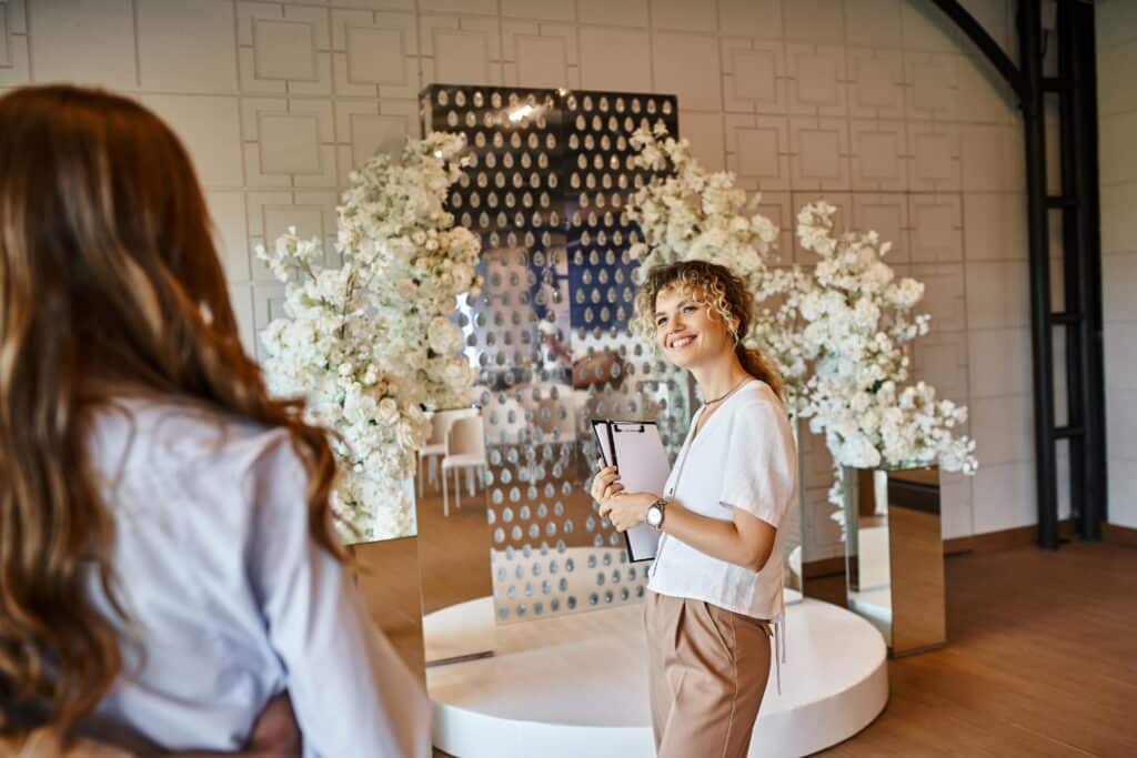 Femme souriante tenant un carnet devant miroir et fleurs